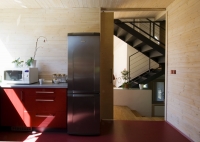 Kuchyň je od obývacího prostoru oddělena posuvnými dveřmi. Odlišuje se také barvou a materiálem. Zatímco v ostatních částech domu převažuje struktura přírodního dřeva, zde architekt použil hladké plochy a výraznou červenou barvu. Podlahu pokrývá marmoleum, linka je vyrobena z lakovaných MDF desek s vysokým leskem.