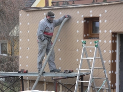 Aplikace foukané celulózové izolace do izolačního prostoru kapsy.