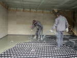 Aplikace cementového potěru Cemflow na rozvody teplovodního podlahového topení. Výšku lité vrstvy „hlídají“ rozmístěné trojnožky (Českomoravský beton).