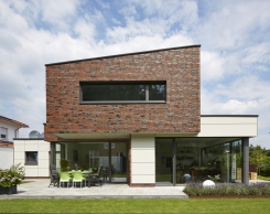 Přízemí rodinného domu s obývákem a jídelnou je velkoryse otevřeno venkovní terase a zahradě díky pevnému zasklení s otvíravě sklopnými okenními dveřmi ze systému Schüco AWS 75.SI. Převis horního patra vytváří praktické zastínění terasy.