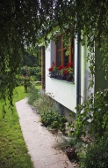  Úzký chodník kolem domu, lemovaný bylinkami, spojuje letní posezení se zahradou.