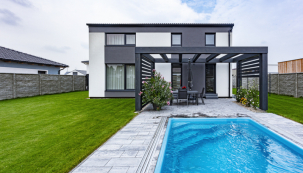 Elegantní kompaktní charakter domu zvýrazňuje kombinace bílé a šedé barvy, kterou dodržuje i dřevěná pergola mořená do šedého odstínu a betonová dlažba na terase
