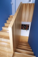 Schodiště architekti navrhli jako kompaktní masivní těleso, zvýrazili jej strukturou dřeva a osvětlením zapuštěným v podstupnicích