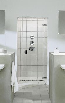 Do sprchového koutu vybudovaného v nice se vchází širokými skleněnými dveřmi. Celý prostor je obložen světlými dlaždicemi a na podlaze se spádem je uprostřed praktická odtoková mřížka