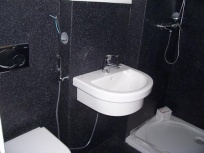 V malé koupelně kontrastuje bílá sanitární keramika oproti černému obložení stěn