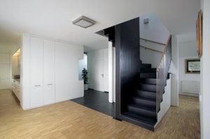 K bílé barvě společenského prostoru zvolil architekt kontrastní kovové schodiště. Nosná konstrukce je obestavěna panelem, který u vchodu slouží jako šatna a z druhé strany jako kuchyňská linka