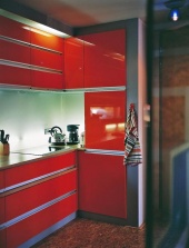 Kuchyňskou linku navrhl architekt z lakovaných MDF desek kombinovaných s hliníkovými prvky. Jako obklad pracovní plochy slouží skleněné desky. Všimněte si originálního osvětlení - v meziprostoru mezi stěnou a sklem jsou instalovány zářivky