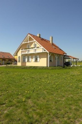 Atraktivní fasáda s podlouhlým balkonem a "neviditelným" proskleným zábradlím. Značný přesah střechy působí jako ozvláštňující prvek a dává vyniknout jak červené krytině Bramac, tak i bíle lakovaným dřevěným prvkům po obvodu konstrukce