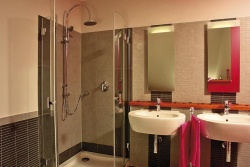 Chladně elegantní rodinná koupelna v odstínech šedé a černé, oživená různým spárováním obkladu. Sanitární předměty jsou od společností Sanitec - Keramag a Kolo