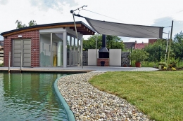 Zahradní domek je stylově sladěn s domem, sezení zastiňuje vypnutá plachta. Do jezírka je zanořený bazén, který neruší romantický ráz okolí