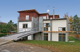 Dynamický architektonický výraz domu vychází z protikladů surových neopracovaných materiálů a perfektně řemeslně provedených prvků. Na fasádě se to projevuje symbióou hrubého pohledového betonu, perfektně vyspárovaného režného zdiva a hladkých omítek
