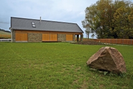 Pohled na dům "za zavřenými vraty". Okna zakrývají posuvné dřevěné panely ze smrkových prken, upevněných na nosné ocelové rámy. Zasouvají se do mezery mezi obvodovou stěnou a kamenným zdivem