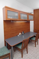 Dlouhý jídelní stůl je osvětlen efektní protáhlou zářivkou stejného typu jako nad pracovní deskou. Kolem stojí čtyři elegantní židle v kombinaci buk/třešeň