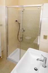 Sprchový kout je uzavřen elegantní posuvnou zástěnou z čirého skla v širokém rámu z nerezové oceli