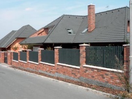 Stupňovitý plot na betonovém základě, pěkně vyzdívaný z lícových cihel se zajímavě kontrastujícími světlými betonovými krycími deskami a osazený hliníkovými plotovými výplněmi (Integra Metal Systems)