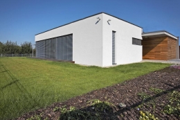 Směrem k jižní straně z architektonické kompozice vystupuje do popředí bílý hladce omítnutý kvádr s velkou prosklenou plochou – ložnicové těleso. Garáž odlišuje obložení cedrovým dřevem. Všechna okna v domě chrání kovové exteriérové žaluzie