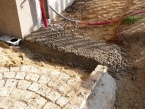 Na podkladovou vrstvu je navezena a lehce srovnána vrstva asi 10 cm polosuchého betonu tak, aby byla o několik centimetrů výš než povrch dlažby