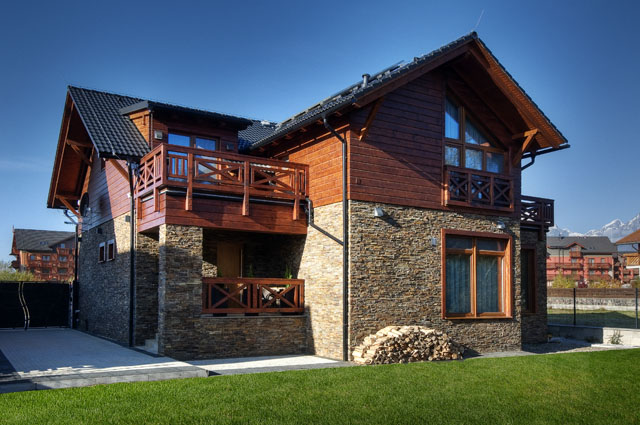 Na fasádách architekt zkombinoval páskový obklad ze štípaného kamene a dřevěné obložení. Je mořeno do kaštanového odstínu, stejně jako zábradlí, podbití a další přiznané dřevěné prvky