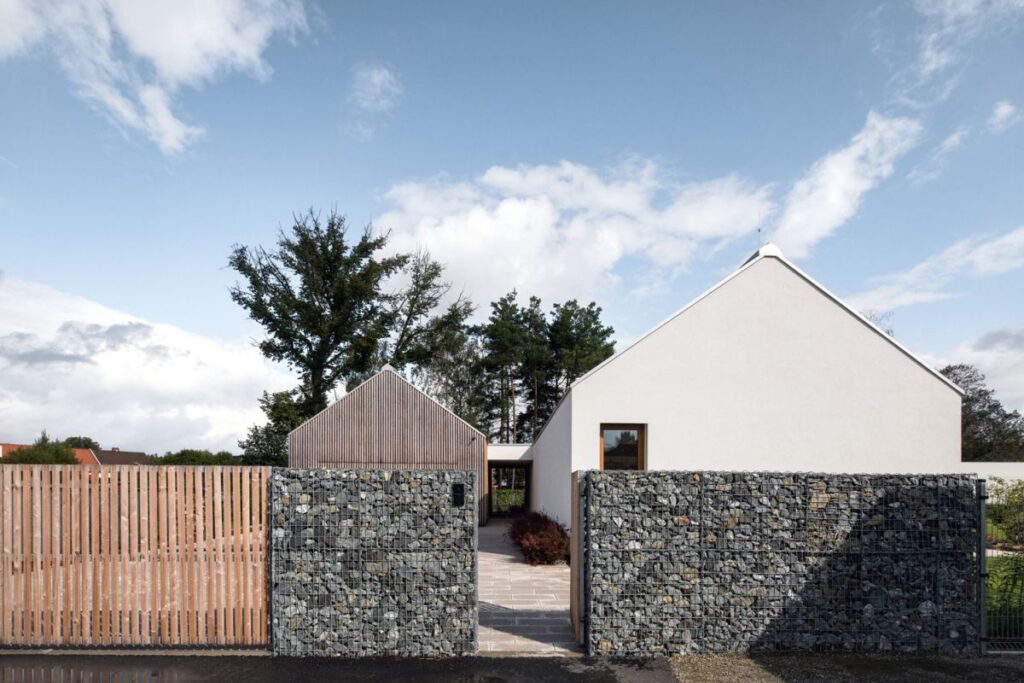 Dům je rozdělen do dvou částí, které propojuje otevřený krček sloužící zároveň jako rozhraní mezi obytnou zónou a garáží s kadeřnickým salonem. Hlavní obytný prostor s kuchyní je otevřený až do krovu